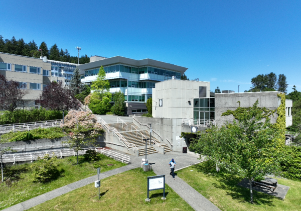 A sprawling landscape with buildings, green grass and trees below a blue sky. 
