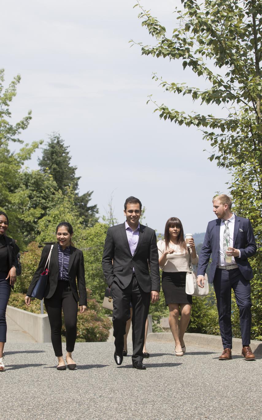 Six students dressed in professional attire walking on a cement path with trees in the background. 