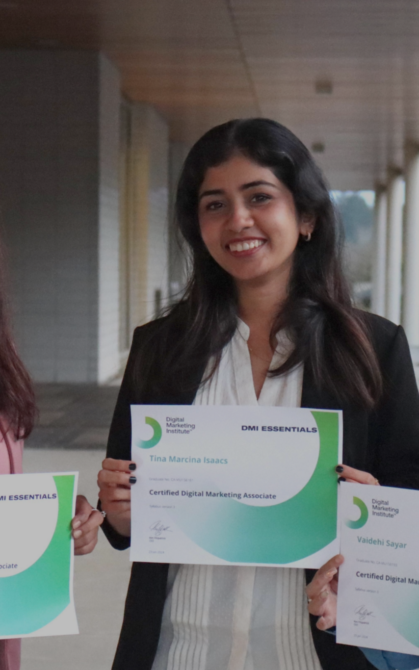 Three smiling female students with long dark hair in casual professional attire holding their DMI certificates