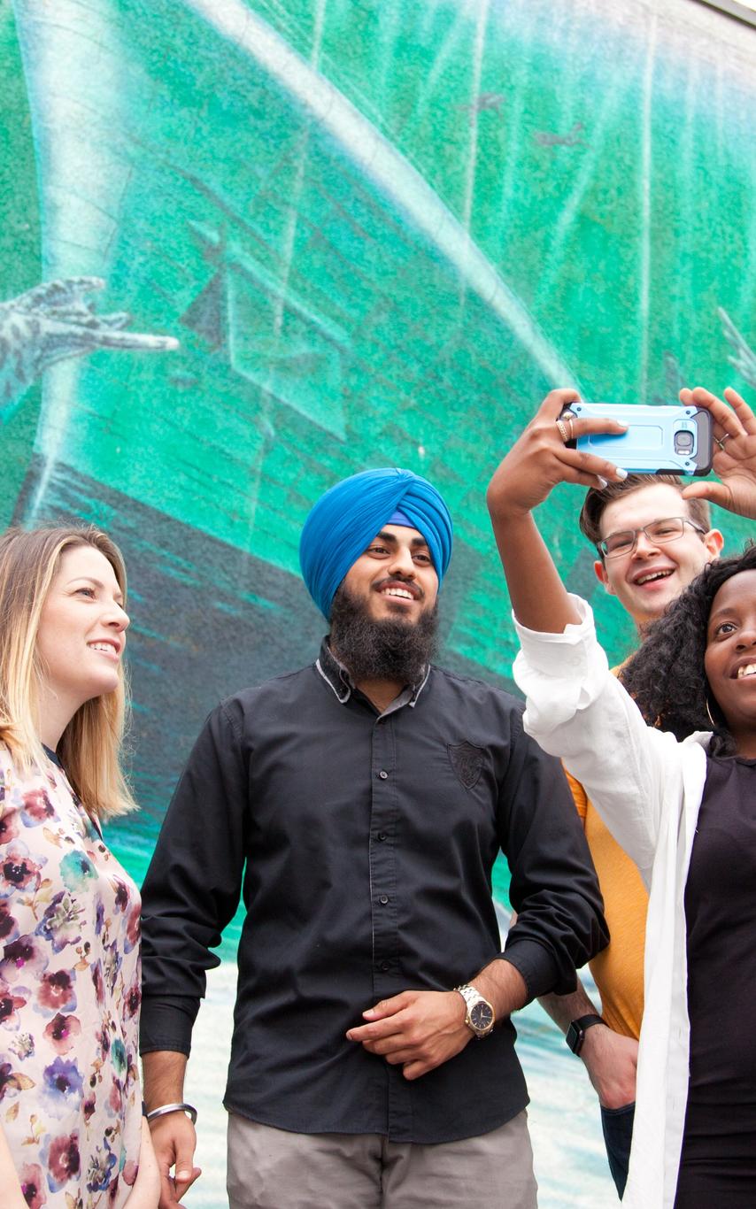 Four students taking a selfie in front of a mural of an underwater scene. 