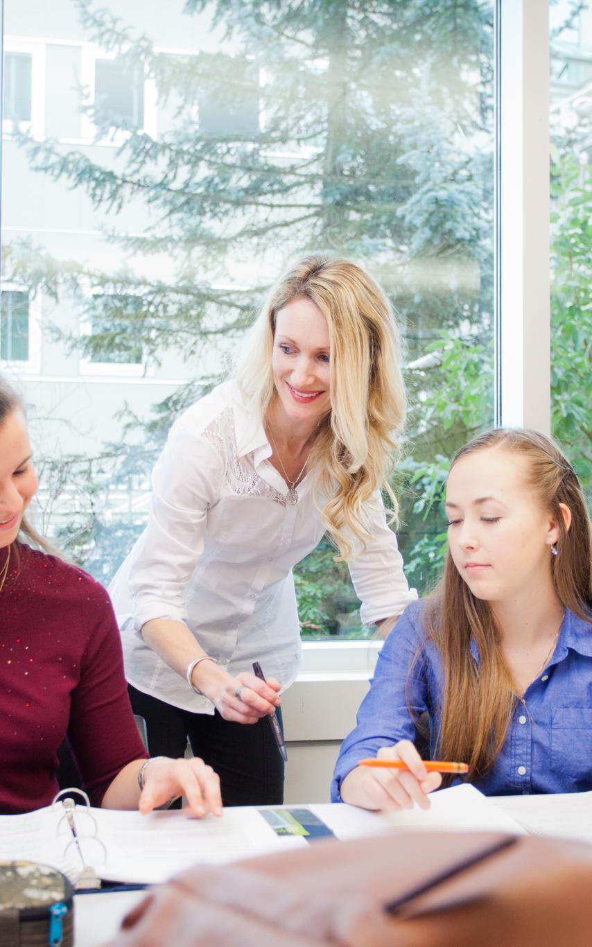 A professor in a dress shirt is leaning over two students working on a project at a table. 